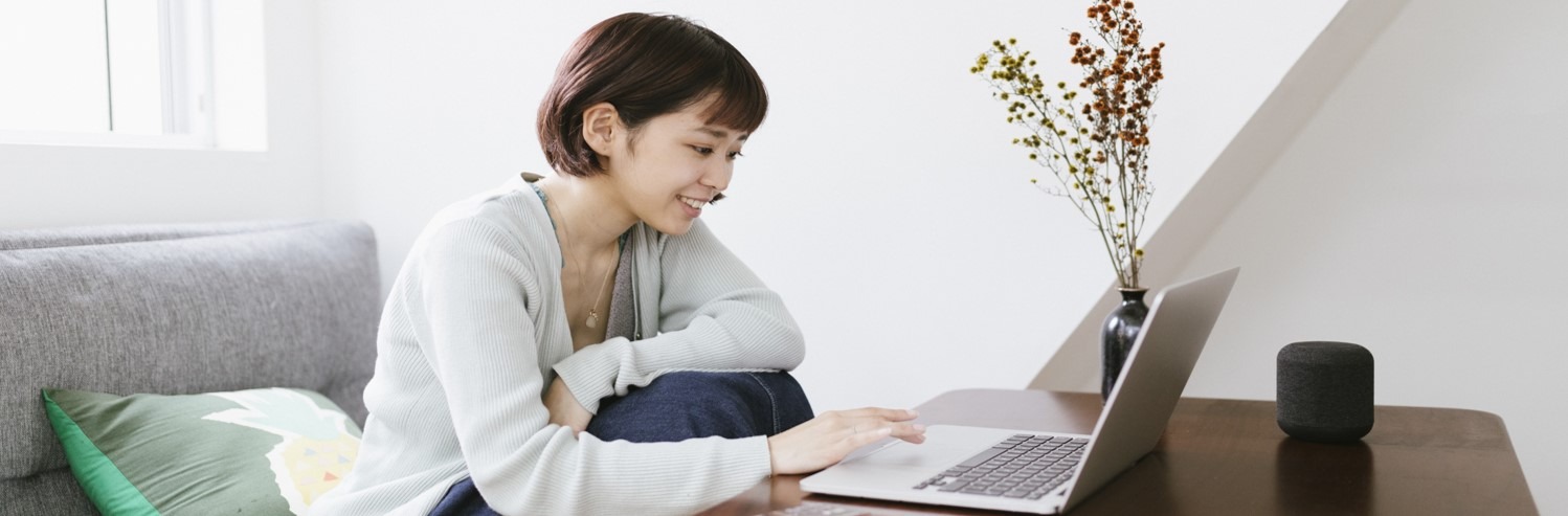 Woman using laptop sitting on grey couch.