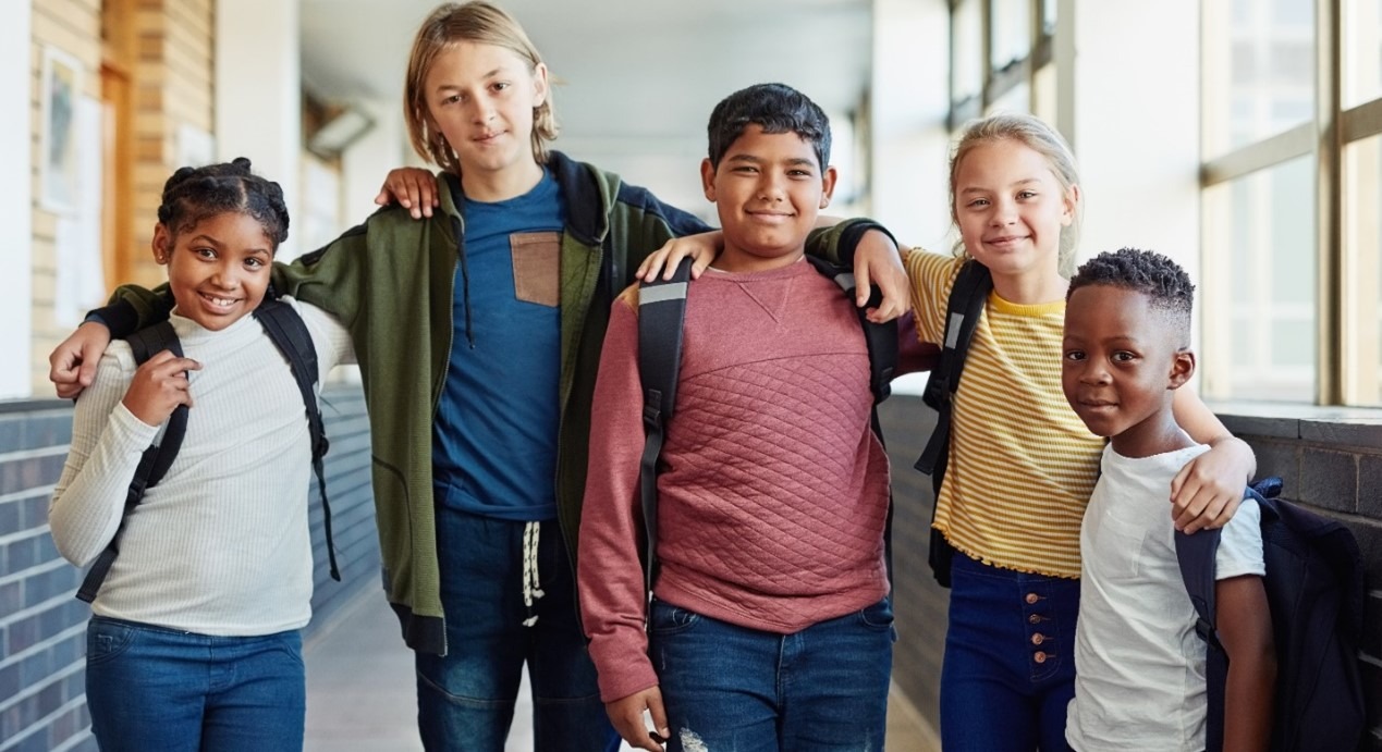 Portrait of five young children with arms on each other's shoulders standing in school hallway